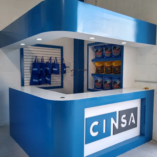 Isla de atención terminada para CINSA: mostrador en L blanco y azul con el logotipo y repisas con producto.