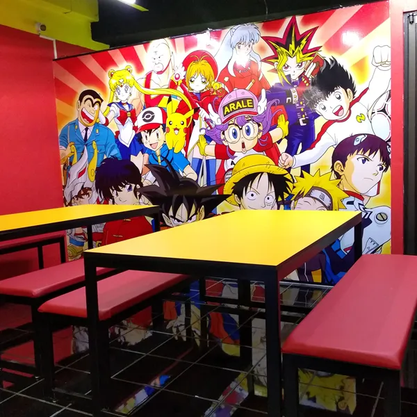 Comedor con mural de personajes de anime, mesas amarillas y bancas rojas.